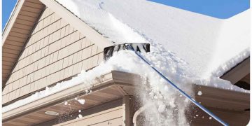 A person is using an ice scraper to clear snow off of the roof.